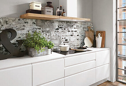 Modern kitchen interior with white cabinetry, stone backsplash, and wooden shelf with decorative items, giving a cozy yet stylish urban home feel.