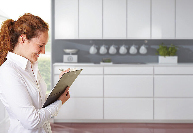 Une femme se trouve dans la cuisine avec la check-list relative à la planification de cuisine.