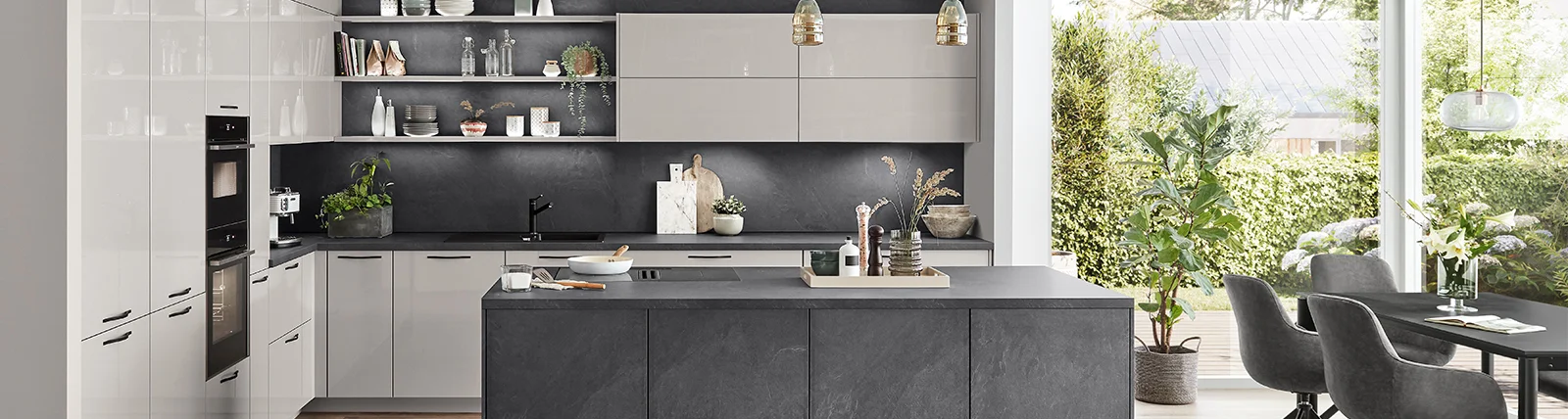 Cuisine contemporaine avec des comptoirs noirs, des armoires blanches, des élégantes suspensions lumineuses et une fenêtre donnant sur un feuillage vert.