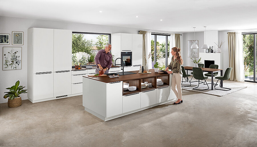 Cocina sofisticada y luminosa con dos personas charlando junto a una isla, con elegantes gabinetes blancos y electrodomésticos contemporáneos.