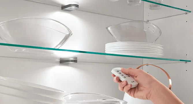 Elegant glass shelving in a kitchen with neatly arranged dishes illuminated by a remote-controlled, adjustable LED lighting system for a modern and sleek look.