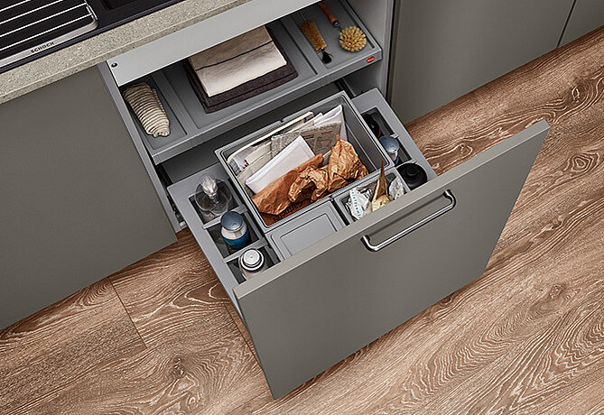 Cajón de cocina moderno abierto mostrando un sistema de almacenamiento bien organizado con compartimentos para utensilios, envolturas de alimentos y otros accesorios de cocina.