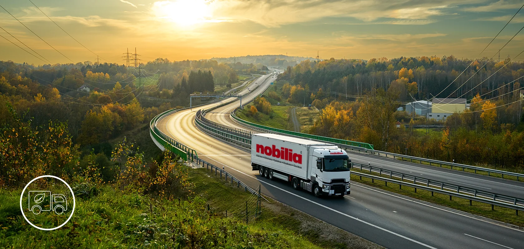 Un camión comercial de la marca "nobilia" viaja por una carretera sinuosa en medio de un vibrante paisaje otoñal con follaje y colinas ondulantes a lo lejos.