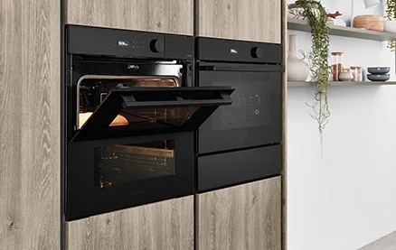 Apparecchio compatto con forno a vapore nella moderna cucina nobilia con frontale RIVA 843 in riproduzione rovere Sierra. Elegante integrazione di elettrodomestici per una preparazione sana e delicata.
