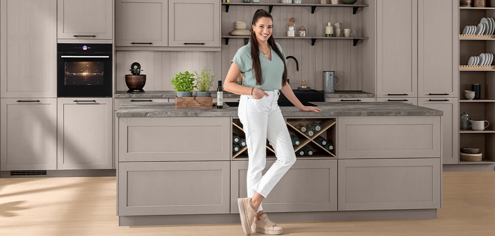 Großzügige Landhausküche mit Kochinsel, warmen Naturtönen und eleganter Linienführung. Die Szene steht für modernes Küchendesign mit viel Stauraum, Funktion und wohnlichem Charakter.