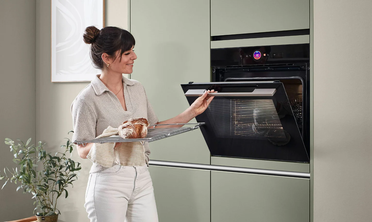 Vrouw voor oven op toegangshoogte in ergonomische keuken - comfortabele en rugvriendelijke bediening