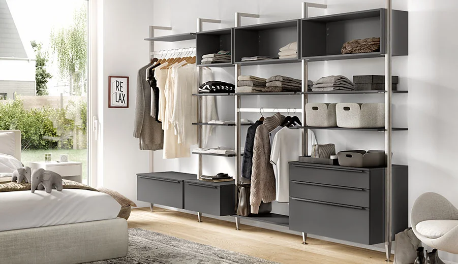 Modernes offenes Kleiderschranksystem in einem hellen Schlafzimmer mit ordentlich organisierten Regalen, hängenden Kleidungsstücken, Schubladen und stilvollen Aufbewahrungsboxen.