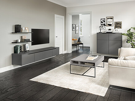 Contemporary living room with a minimalist design, featuring sleek furniture, neutral colors, and a well-organized entertainment unit against a gray wall.