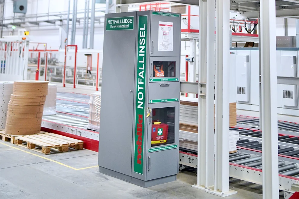 Notfallstation mit Erste-Hilfe-Ausrüstung und Defibrillator in einem Industrielager installiert, um die Arbeitssicherheit zu verbessern und die Bereitschaft für medizinische Notfälle zu erhöhen.