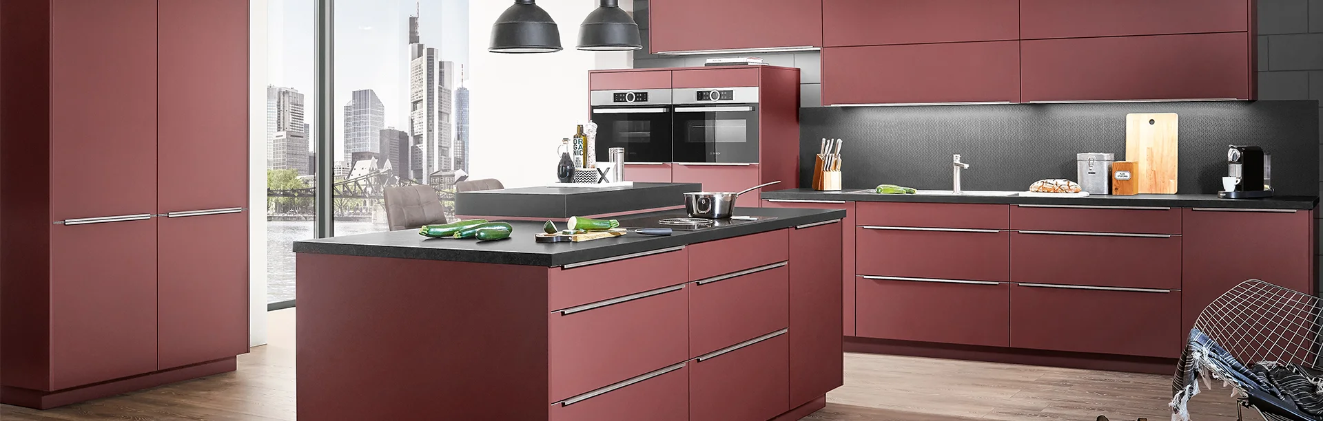 Nowoczesna kuchnia bez uchwytów z frontem EASYTOUCH 963 w kolorze rdzawoczerwonym ultra matowym i czarnym blatem, miejska atmosfera z widokiem na panoramę miasta.
