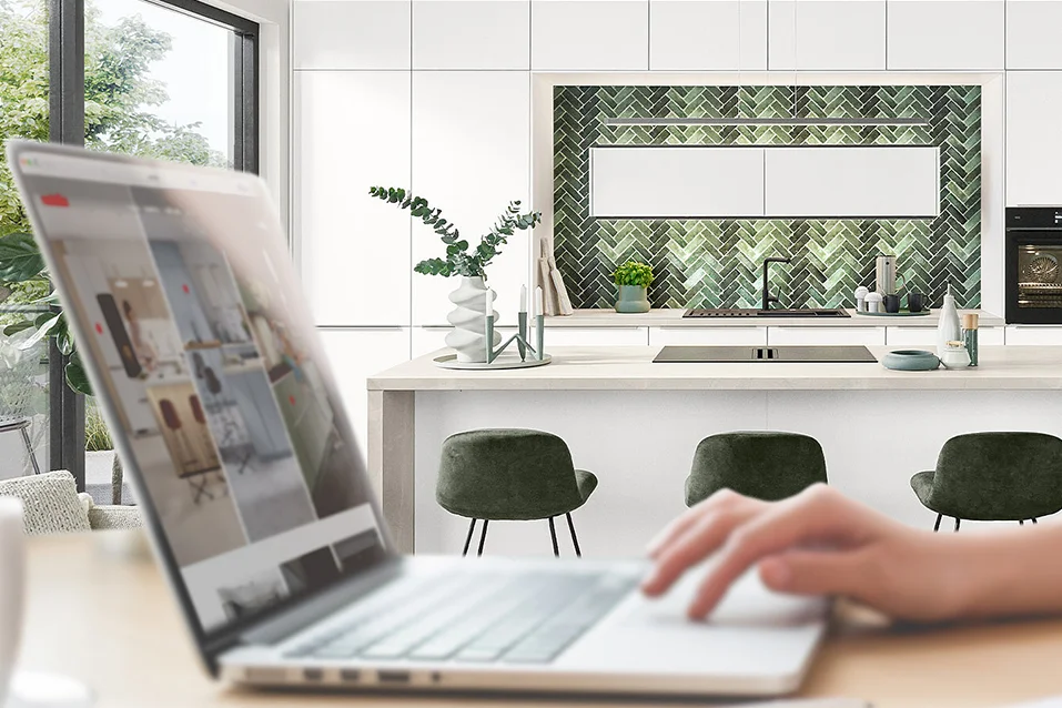 Laptop im Vordergrund, weiße Küche Softline 507 mit Kücheninsel und grünem Fliesenspiegel im Hintergrund