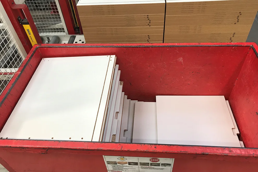 Pila de piezas de muebles desmontados organizados en un contenedor de metal rojo listo para ensamblar o transportar, visto en un entorno de almacén.