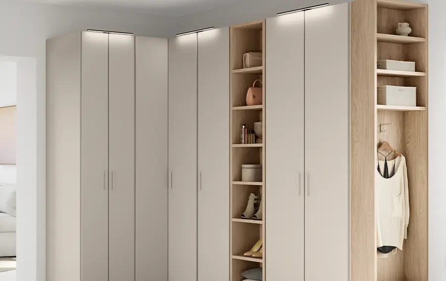 Aufsatzbeleuchtung an einem Schlafzimmerschrank mit hellen Fronten und offenen Regalfächern in Holzdekor