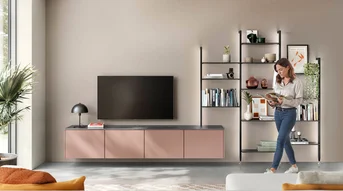 Wohnzimmer in Koralle mit beleuchtetem Stollenregalsystem, TV-Möbel und offenem Regal im Wohnbereich.