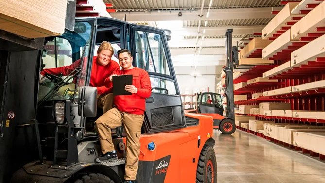 Zwei Auszubildende als Fachlageristen in der Produktionslogistik, die an einem Gabelstapler arbeiten und Lagerbestände kontrollieren.