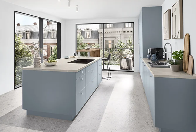 Jasna kuchnia z frontem SENSO 485 w matowym kolorze Sky Premium i jasnym blatem, nowoczesny wygląd z dużymi oknami i widokiem na kamienice.