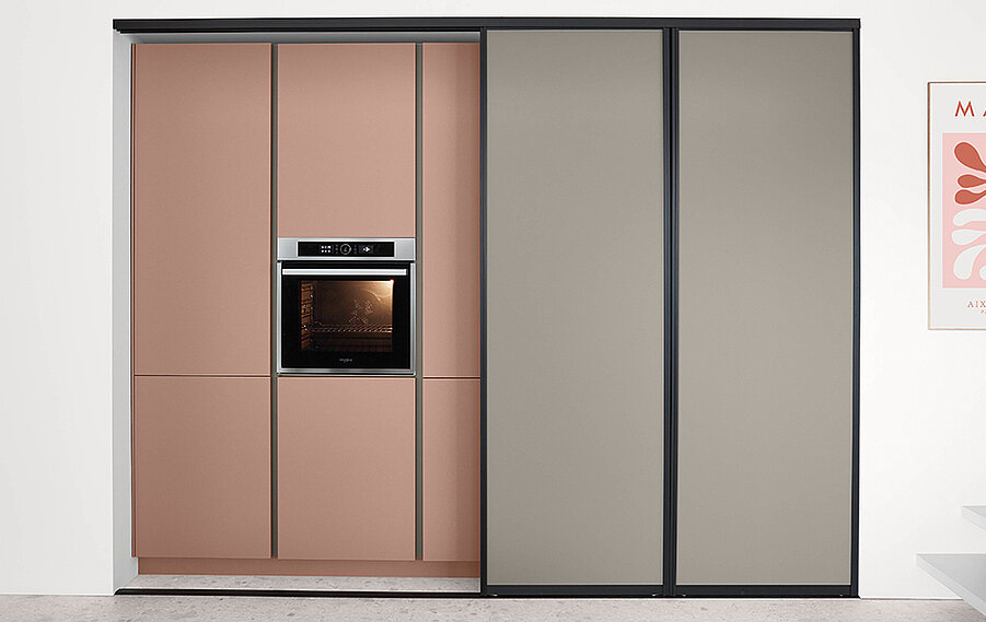 Moderní kuchyňská skříň s vestavěným troubou, která předvádí elegantní design s posuvnými dveřmi v růžové a šedé barvě a minimalistickým stylem v moderním interiéru.