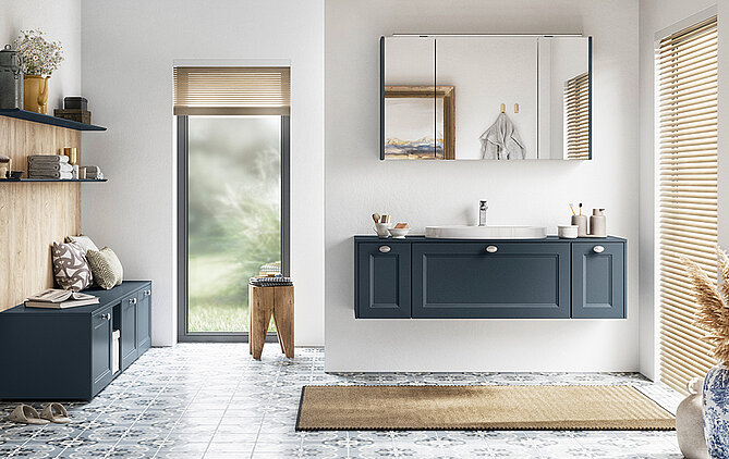 Elegantní koupelnový interiér obsahuje dvojitou umyvadlovou skříňku v klasickém modrém odstínu, doplněnou dlažbou a klidným výhledem inspirovaným přírodou.
