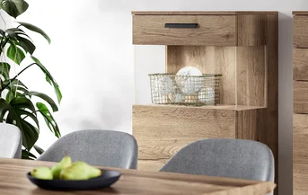 Interior moderno de comedor con elegantes sillas grises, aparador de madera y plantas decorativas, resaltando un diseño minimalista y texturas naturales.