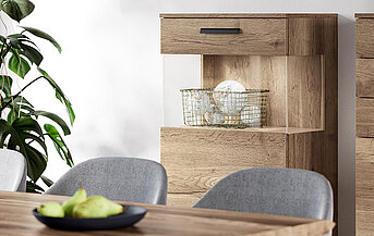 Modernes Esszimmer-Interieur mit eleganten grauen Stühlen, einem Holz-Sideboard und dekorativen Pflanzen, die minimalistisches Design und natürliche Texturen betonen.