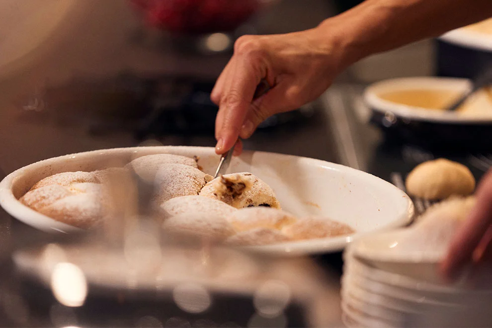 Eine Nahaufnahme einer Person, die köstlich aussehende Desserts in einer warmen, intimen Kücheneinstellung mit Puderzucker verziert.