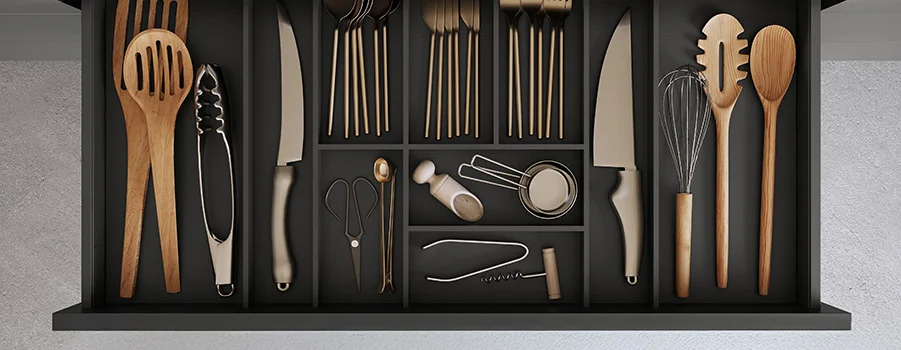 Una variada selección de utensilios de cocina de madera y acero inoxidable dispuestos sobre un fondo negro.