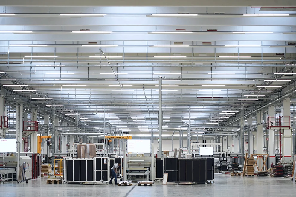 Modern industrial warehouse with a clear, organized space featuring high ceilings, storage racks, and a worker overseeing operations in a vast facility.