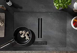 Moderní indukční varná deska s elegantním designem, na které je jedna pánev s houbami obklopená minimalistickými kuchyňskými náčiním a čerstvými bylinkami.