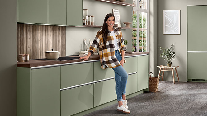 Front SENSO 495 in Olive Premium matt – präsentiert von Markenbotschafterin Sally in einer modernen, wohnlichen Küchenumgebung.