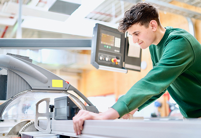 Ein junger Mann bedient eine moderne Schneidemaschine in einer hellen Werkstatt und konzentriert sich auf seine Tischler- oder Ingenieuraufgabe.