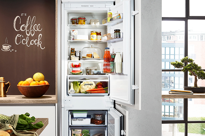 Gezeigt wird ein Ausschnitt einer JUNKER Kühl-Gefrierkombination in einer nobilia Küche, die geöffneten Türen geben den Blick auf eingeräumte Lebensmittel frei 