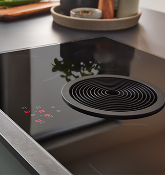 Moderne Induktionskochplatte mit Touch-Bedienung und elegantem Design, auf deren glänzender schwarzer Oberfläche Kochgeschirr und Utensilien subtil reflektiert werden.