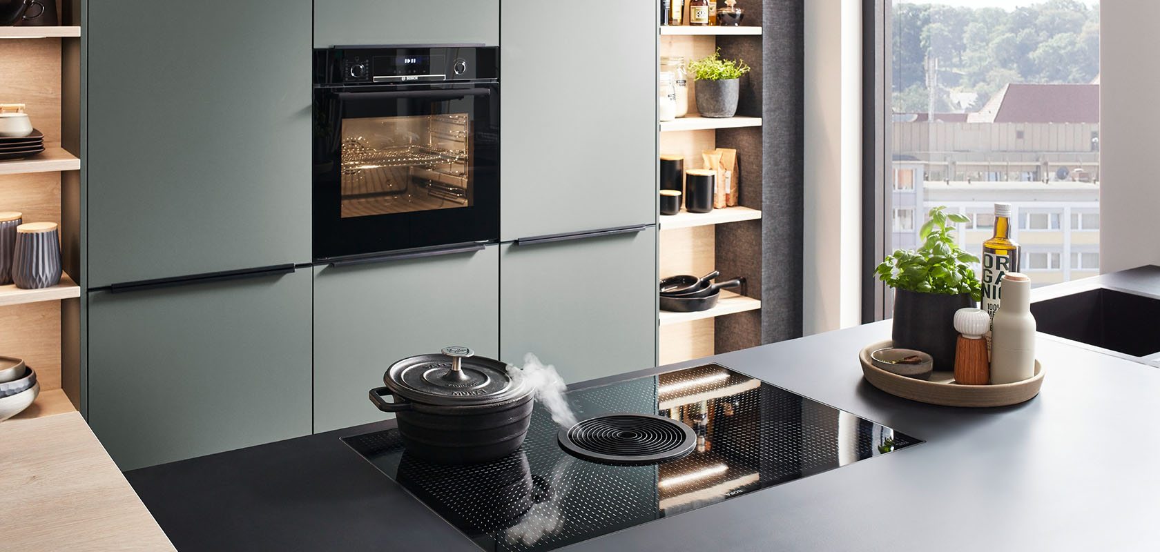 Interior de cocina moderna con elegantes gabinetes verdes, electrodomésticos integrados y una placa de inducción en una encimera oscura, que emana estilo y funcionalidad contemporáneos.