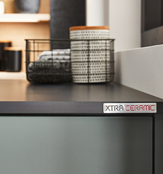 Modern kitchen detail showcasing a sleek countertop with the logo "XTRA CERAMIC," accompanied by stylish storage baskets and cozy, minimalist decor in a tranquil setting.