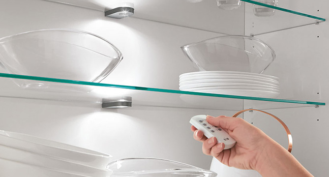 Elegantní skleněné police v kuchyni s pečlivě uspořádaným nádobím osvětleným dálkově ovládaným, nastavitelným LED osvětlením pro moderní a elegantní vzhled.