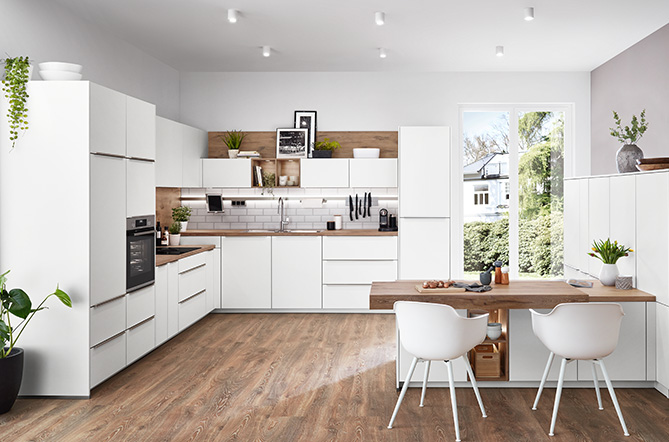 Helle L-Küche mit Front Senso 488 in Weiß Premium matt, kombiniert mit Holzarbeitsplatte und integrierter Sitzgelegenheit, modernes und natürliches Ambiente mit klarer Linienführung und wohnlichem Charakter.