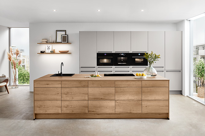 Moderne Küche mit Front Softline 508 in Seidengrau Perfect matt, kombiniert mit einer großzügigen Kochinsel in Holzoptik, elegantes Design mit grifflosen Fronten und harmonischem Farbspiel aus Grau und Naturtönen.