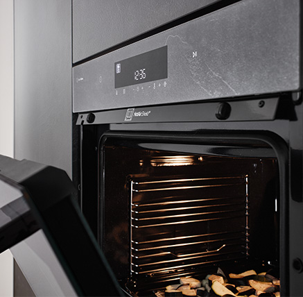 Laurus Backofen in Grauschiefer Nachbildung passend zur Küchenfront Stoneart 303 geöffnet mit aktivem HotAirShield und weißer Displayanzeige für moderne Backtechnologie in harmonischem Design