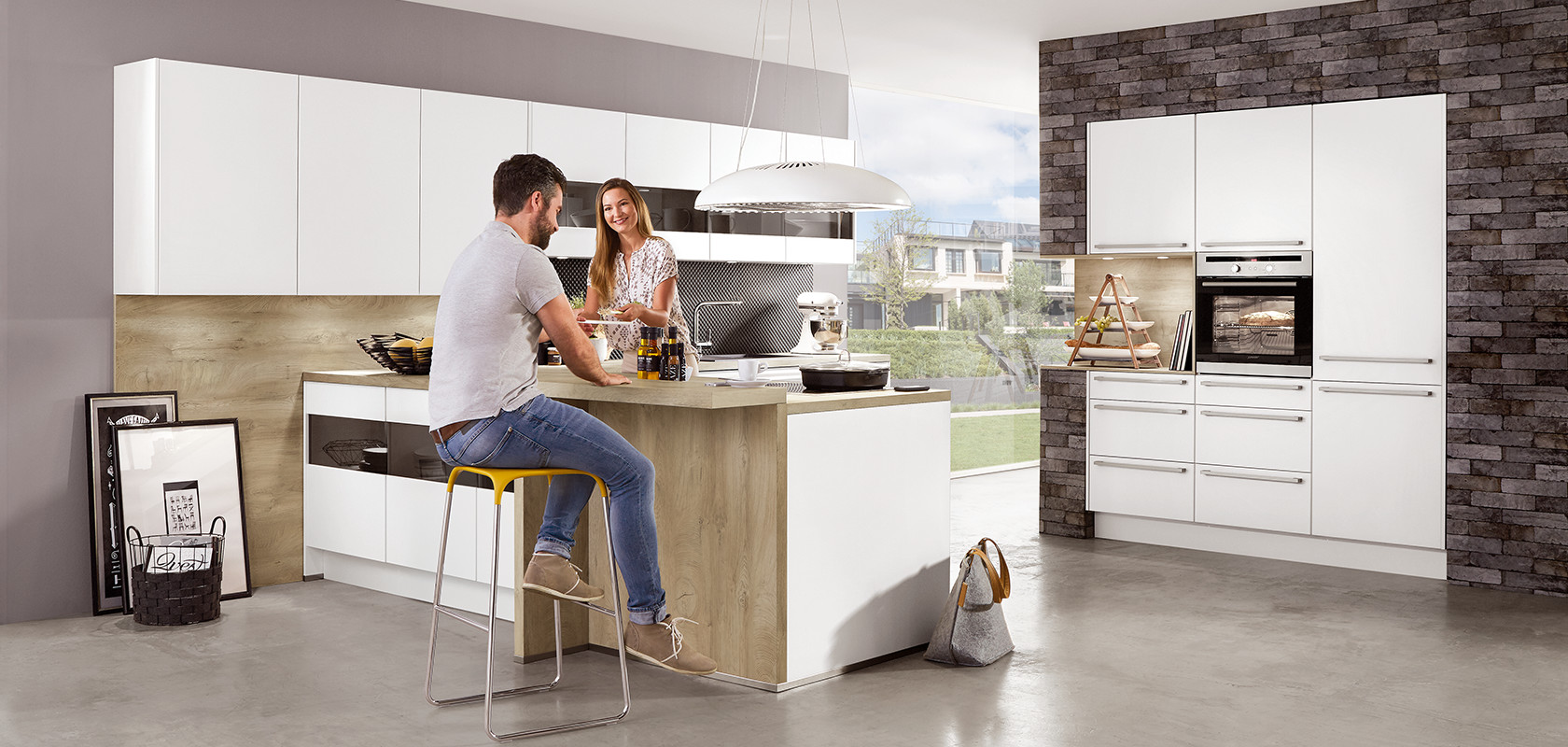 A modern kitchen setting with a smiling couple engaging over a meal prep island, featuring sleek appliances and minimalist design aesthetics.