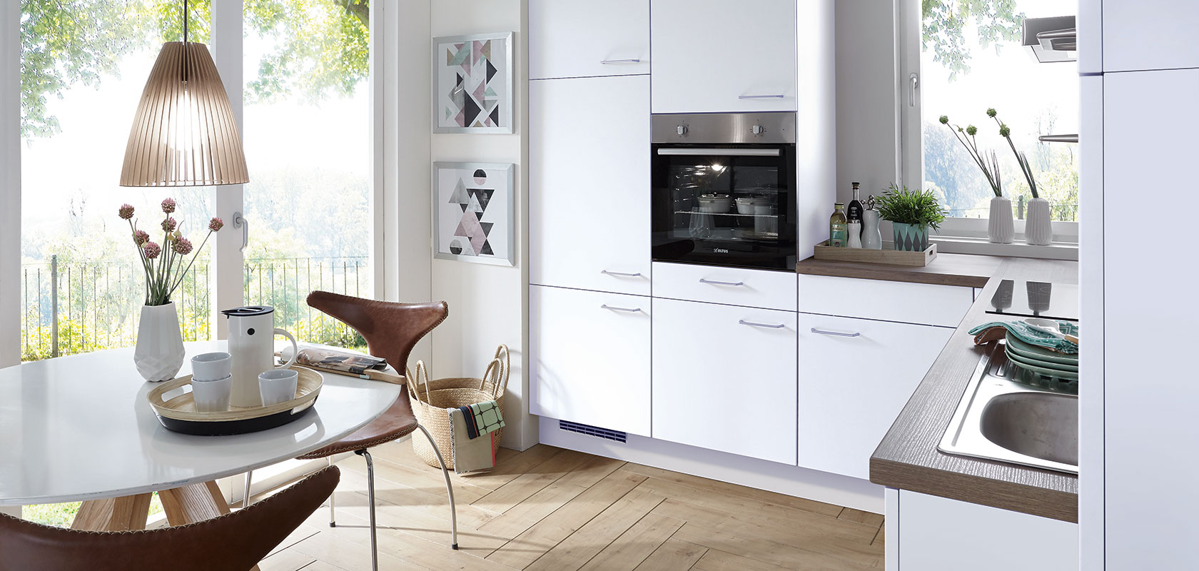 Luminoso y moderno interior de cocina con gabinetes blancos limpios, electrodomésticos integrados y un acogedor comedor con una mesa redonda con vistas a un soleado jardín.