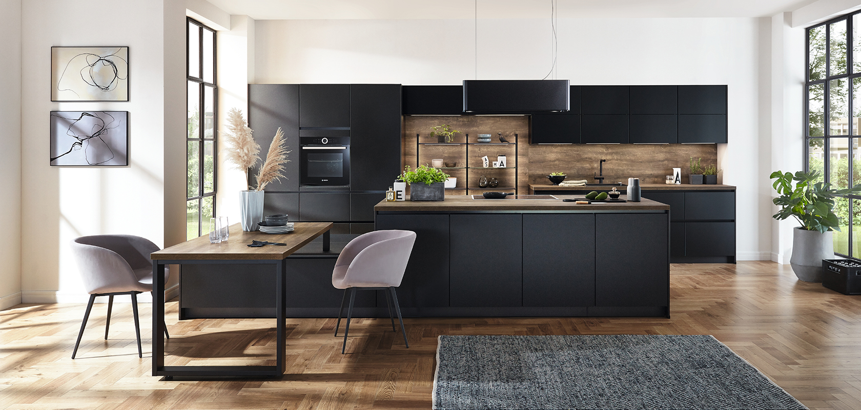 Interior de cocina moderna que muestra elegantes gabinetes negros, acentos de madera y una isla espaciosa complementada por luz natural de grandes ventanas.
