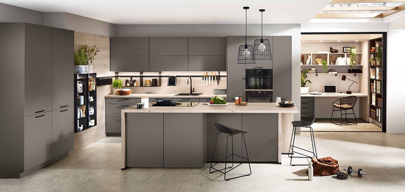 Diseño de cocina moderna con gabinetes grises elegantes, electrodomésticos integrados y una isla con taburetes, que se extiende sin problemas a un acogedor rincón de oficina en casa.