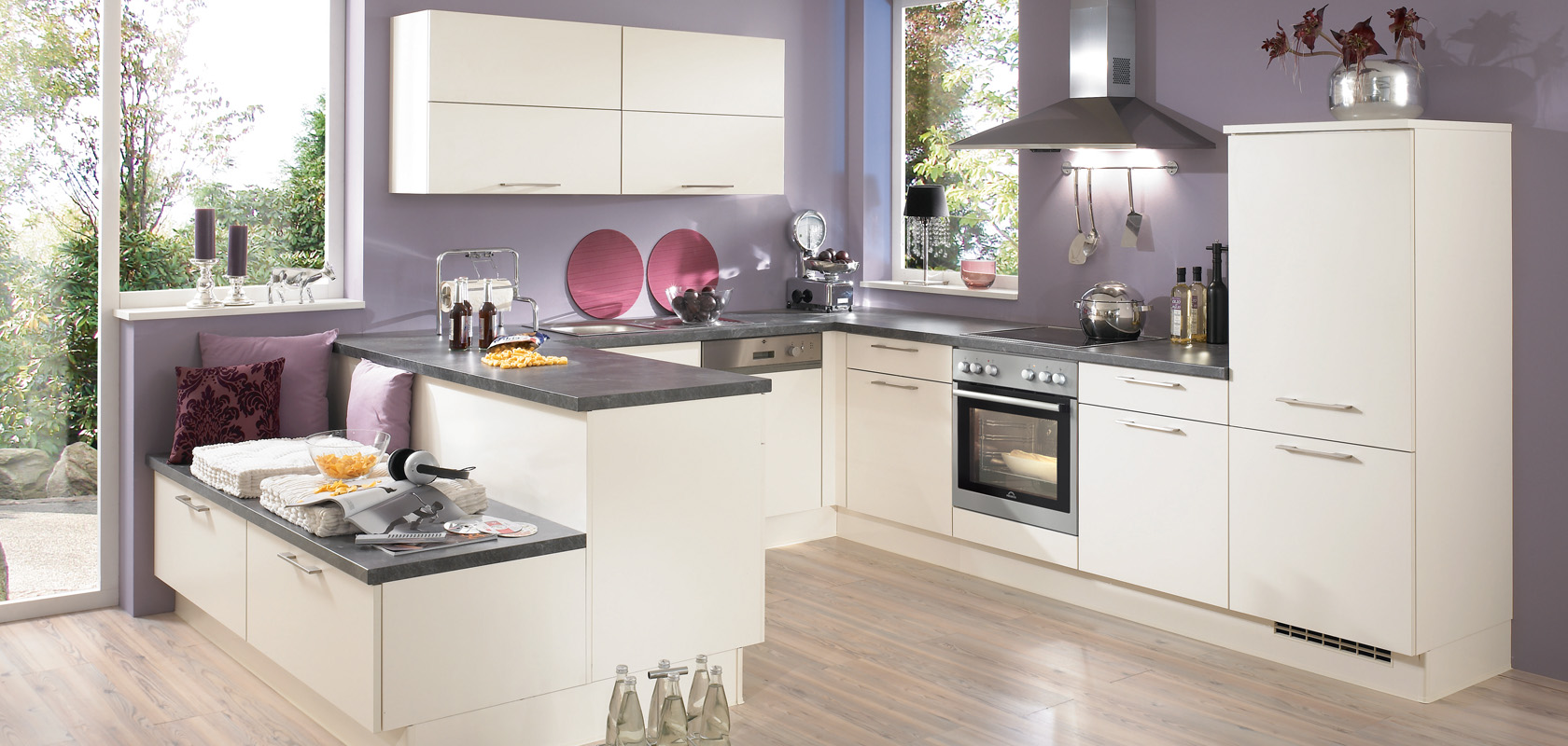 Moderne keuken met strakke witte kasten, donkere werkbladen en roestvrijstalen apparaten, aangevuld met natuurlijk licht en een knusse eethoek.