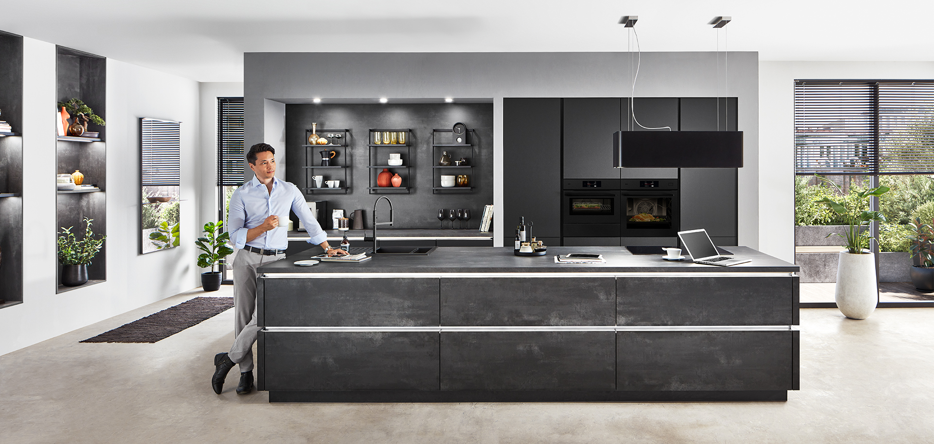 Interior de cocina moderna con un diseño elegante con gabinetes negros, electrodomésticos integrados y una persona preparando comida en la encimera de la isla.