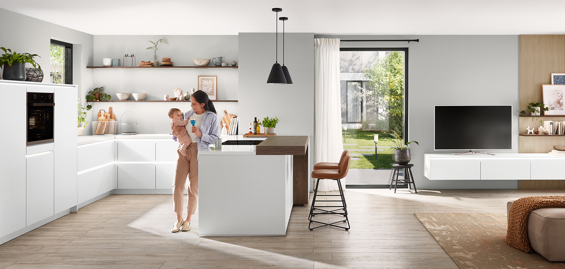 Intérieur de cuisine moderne avec un design propre et minimaliste comprenant des armoires blanches, un îlot central et une jeune mère tenant affectueusement son enfant.
