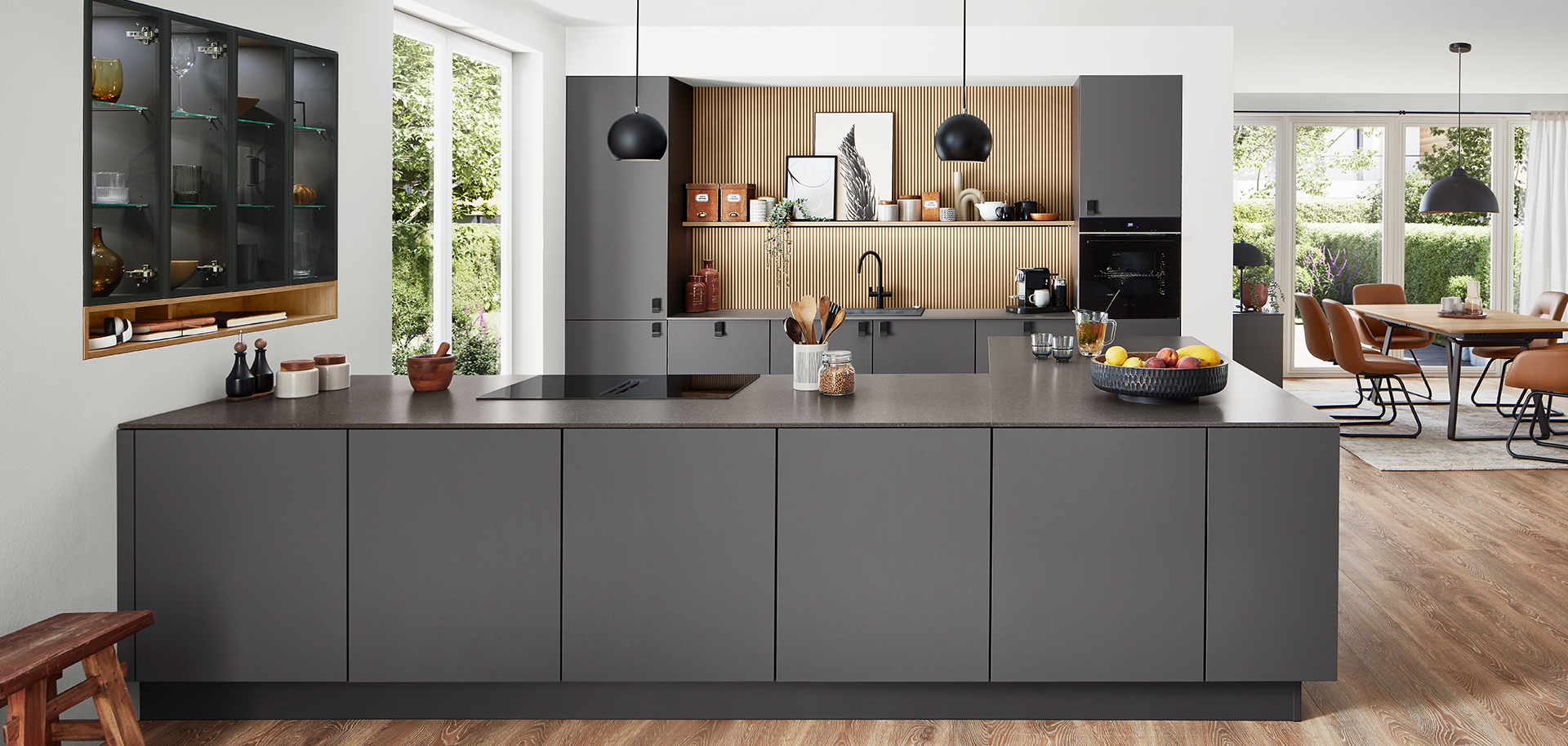 Cocina moderna con elegantes gabinetes negros, electrodomésticos integrados y una isla central, que se integra perfectamente con un luminoso y espacioso comedor.