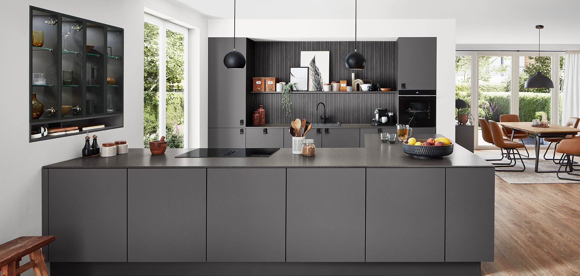 Modern kitchen featuring sleek black cabinets, built-in appliances, and a central island, seamlessly integrating with a bright, spacious dining area.