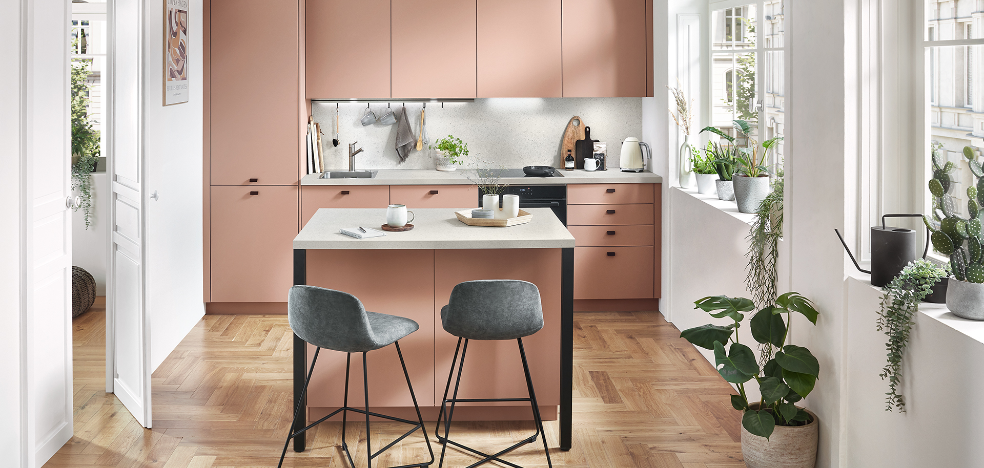 Una cocina moderna y espaciosa con elegantes gabinetes blancos, electrodomésticos de acero inoxidable y un acogedor comedor con sillas grises elegantes y plantas verdes exuberantes.