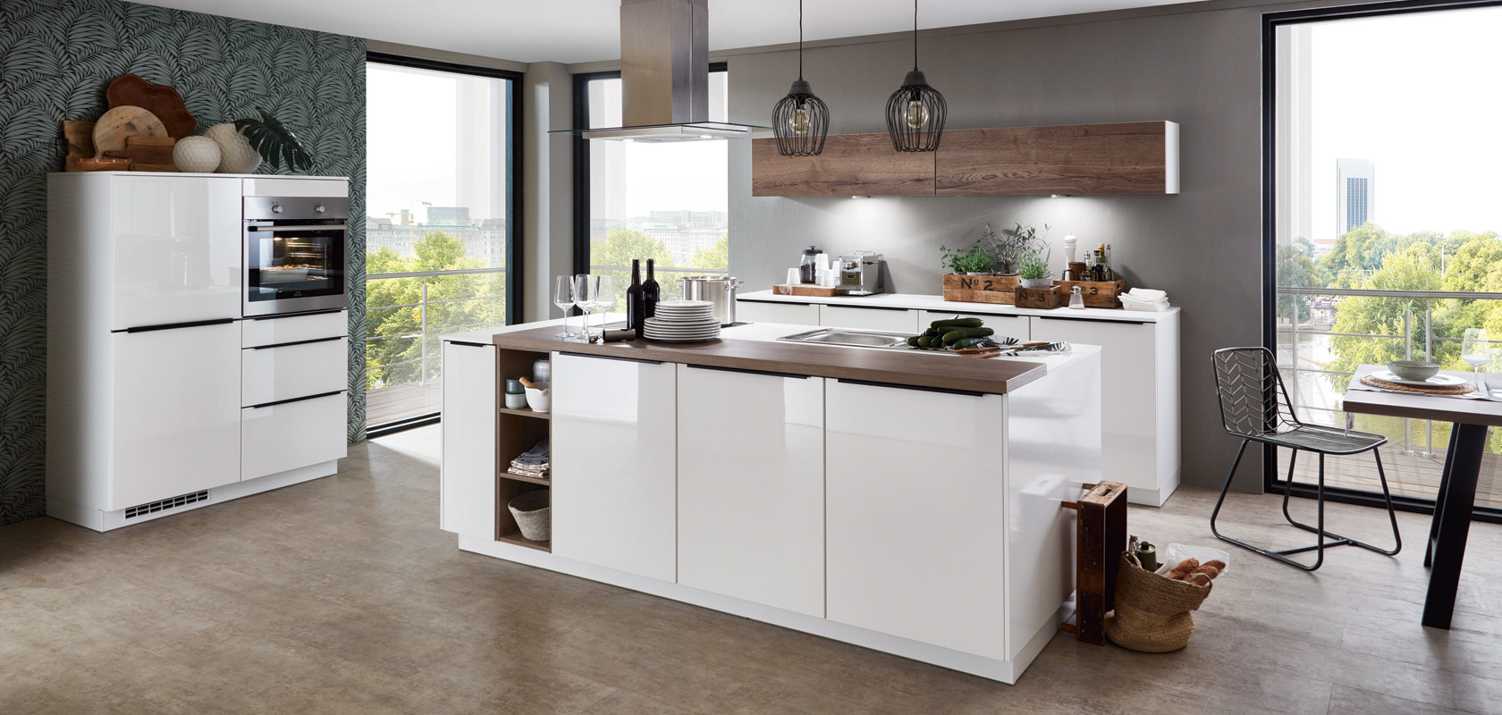Modern kitchen interior featuring white cabinetry, integrated appliances, and a central island with a cooktop, set against a backdrop of large windows and greenery.