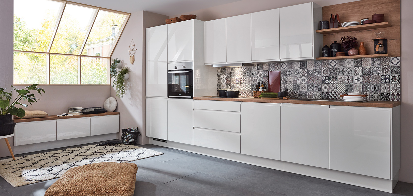 Moderní kuchyňský interiér s čistými bílými skříněmi, geometrickými obklady na zdi a dřevěnými detaily, které vytvářejí útulný a stylový prostor pro vaření a pobyt.